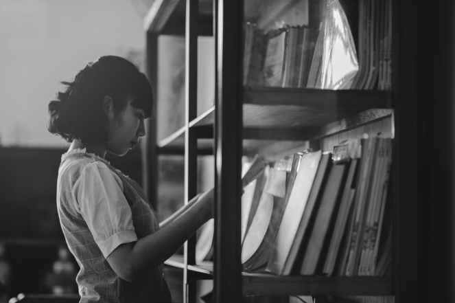 grayscale photo of a woman holding a book inside the library