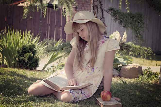 girl in white and blue dress reading books while sitting on lawn