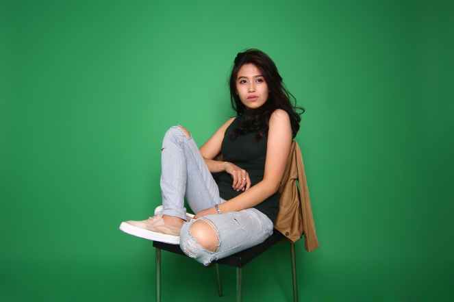 woman wearing black sleeveless top and distressed blue denim jeans outfit while sitting on chair
